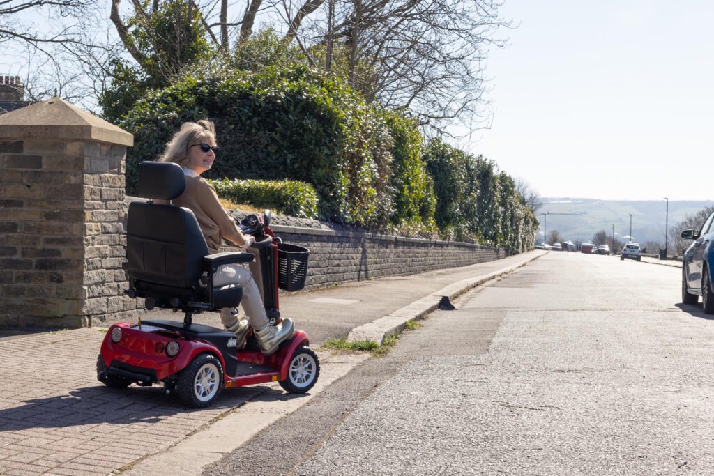 A woman riding a mobility scooter along an empty pavement, looking to her right in order to drive onto a road