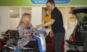 man showing a lady howe to use a mobility scooter in a showroom