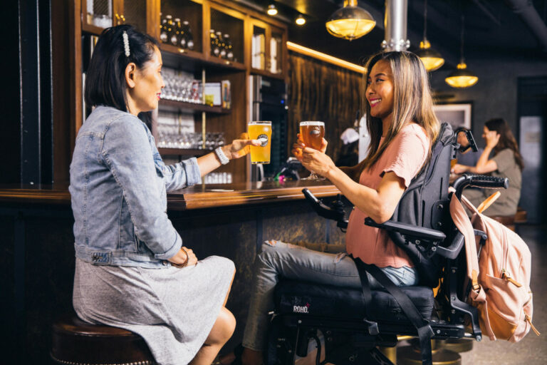 two ladies sitting in a bar with glasses of beer - one in a powerchair