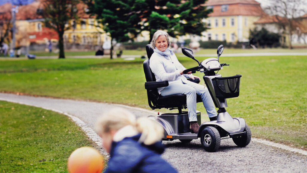 older lady sitting in a mobility scooter smiling at a little girl playing with a ball