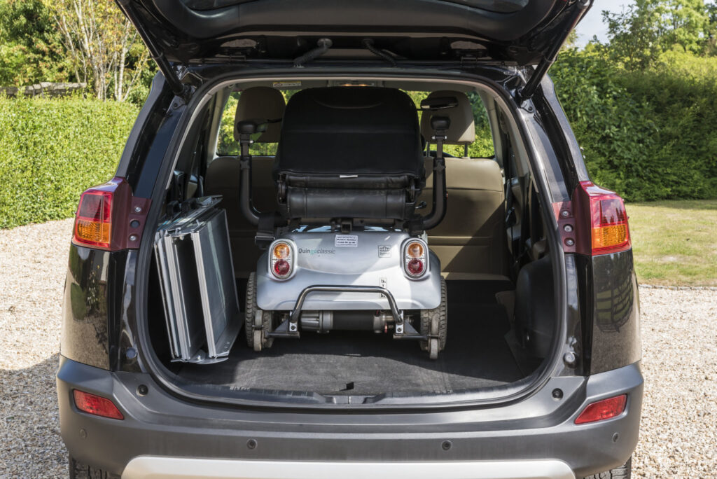 a scooter and a portable, foldable ramp in the boot of a car