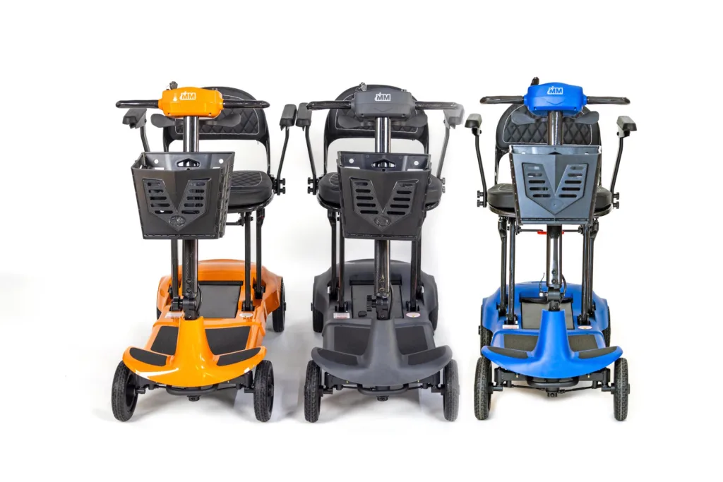 Three Genie mobility scooters in a row - one in orange, one in grey and one in blue