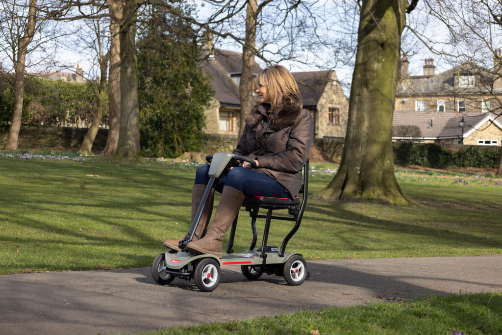 A woman riding an Air mobility scooter along a path in a park
