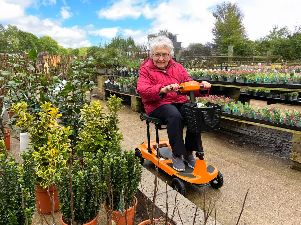 Elderly lady riding a Genie Utra Light mobility scooter in a garden centre