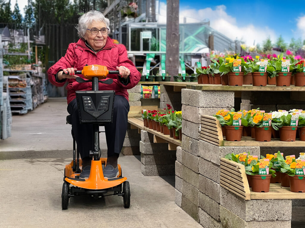 an elderly lady riding a Genie Ultra Light mobility scooter in a garden centre