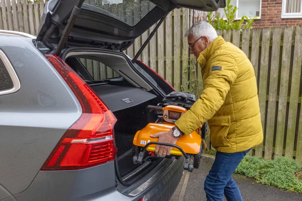 Gentleman placing a folding mobility scooter into the boot of his silver car