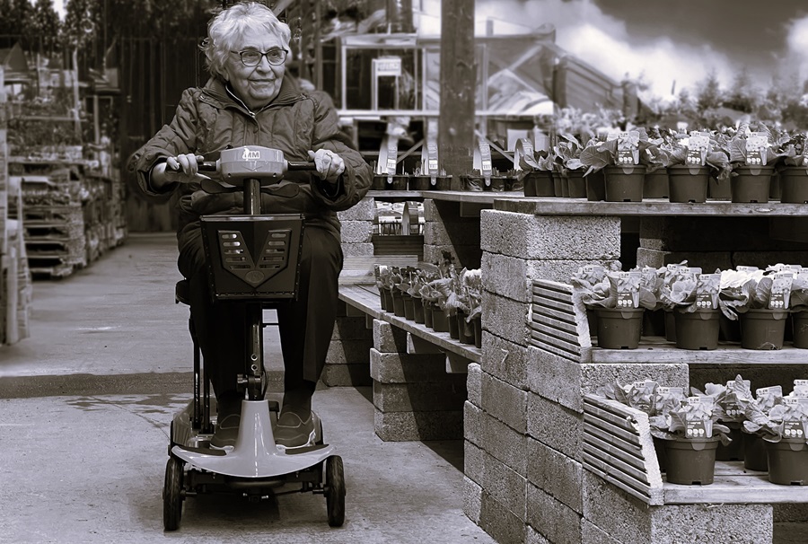 Black and white photo of an elderly lady on a mobility scooter in a garden centre