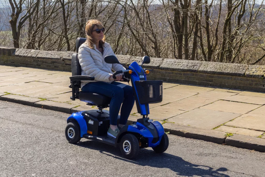 side view of a lady driving a blue MM8 mobility scooter on a road on a sunny day