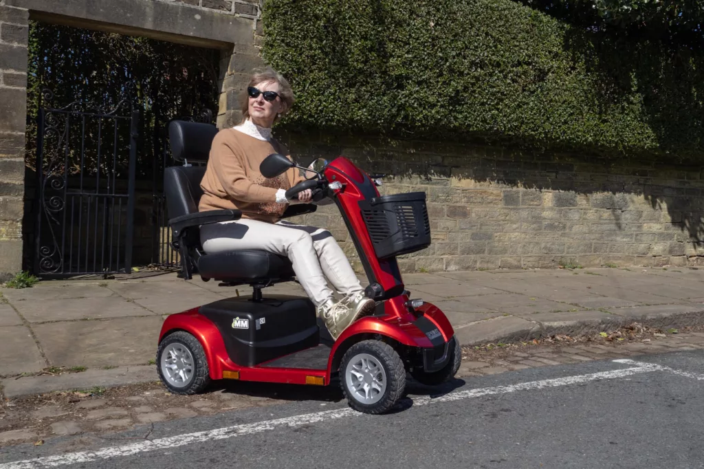 a woman on a red mobility scooter looking to the right as she crosses a road
