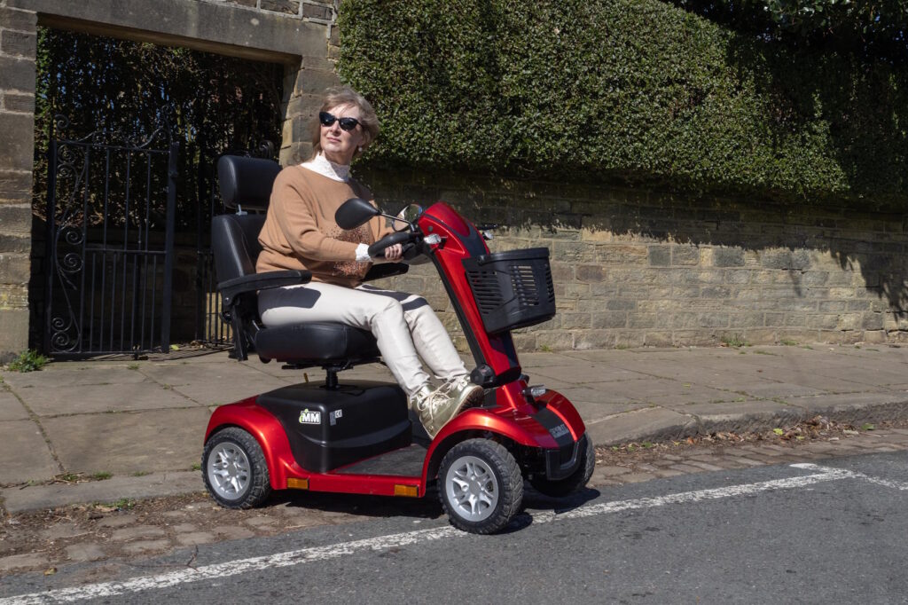 a woman on a red mobility scooter looking to the right as she crosses a road