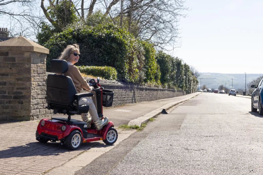 a woman riding a mobility scooter along an empty pavement, looking to her right in order to drive onto a road