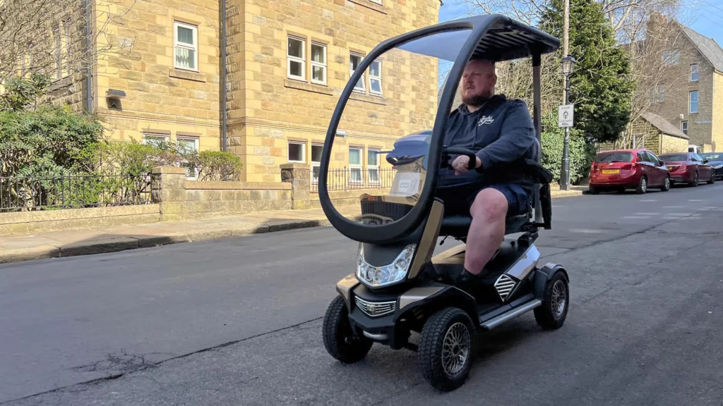 Front view of a large man riding the Storm mobility scooter down a residential road