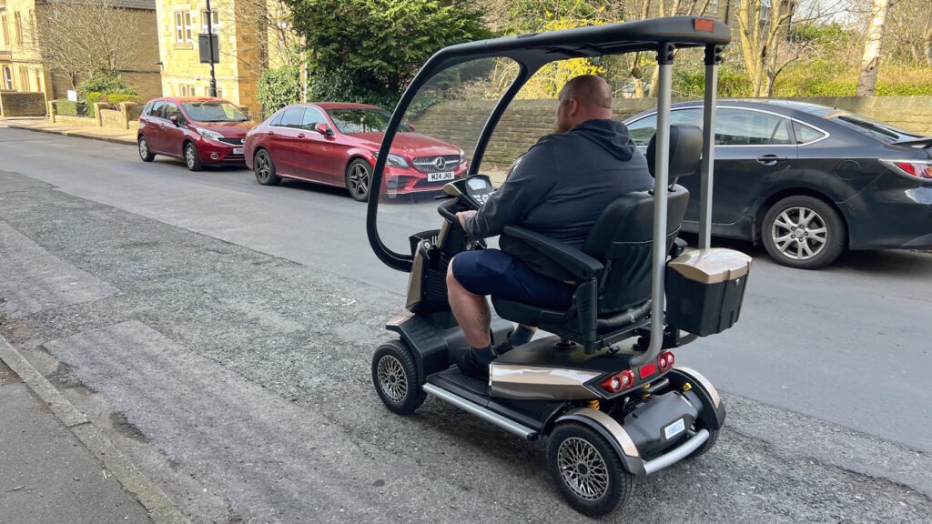 Side view of a larger man riding the Storm mobility scooter down a quiet road