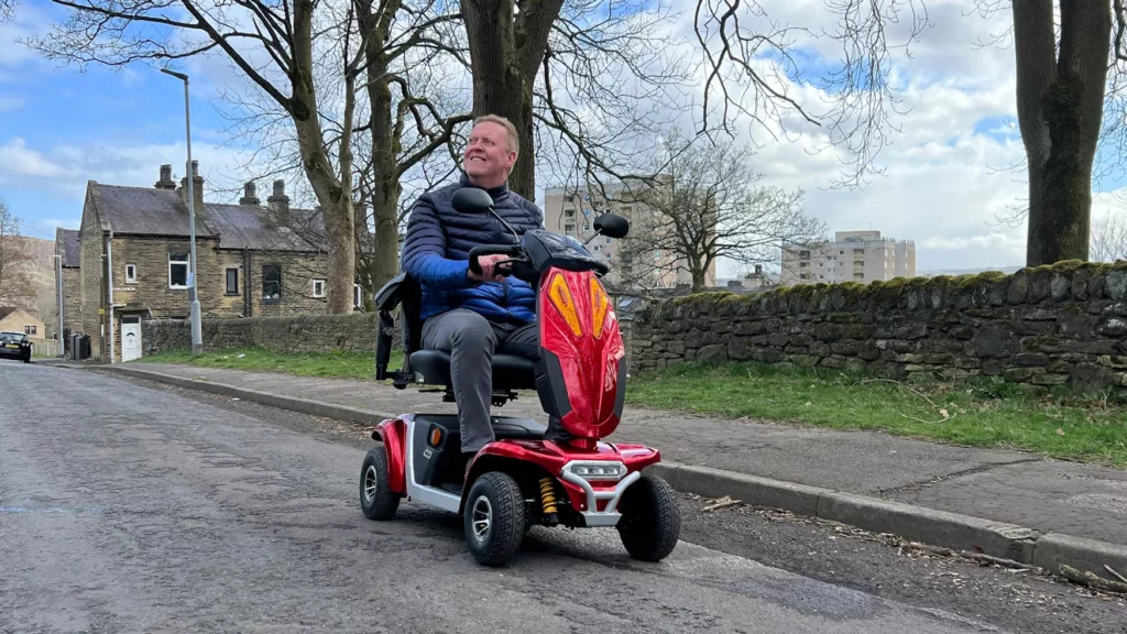 Man on a red mobility scooter driving along a quiet road