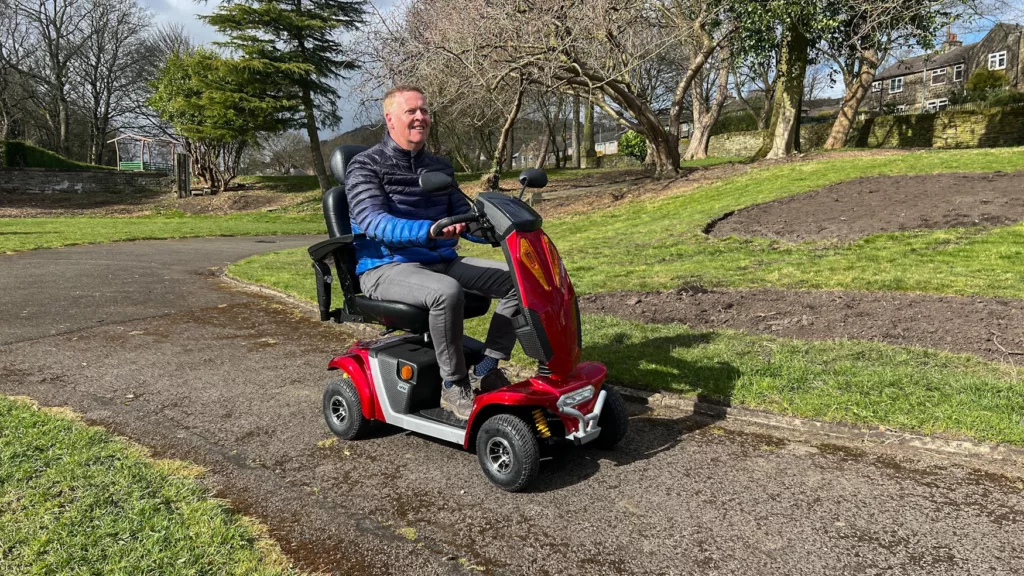 Gentleman driving a red mobility scooter in a park