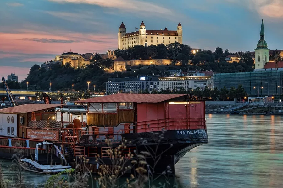 A view of Bratislava at dusk with a boat in the foreground and the castle in the background