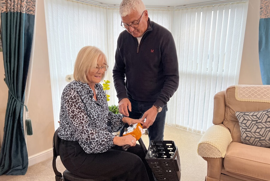 Gentleman showing a lady how to use a mobility scooter inside her sitting room