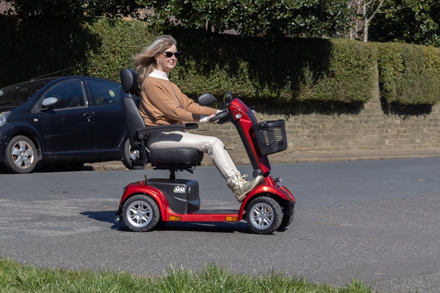 Lady driving a red mobility scooter along a residential road
