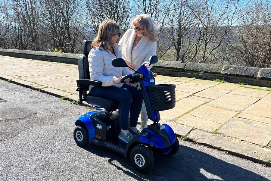 Lady on a blue mobility scooter chatting to a friend on the pavement