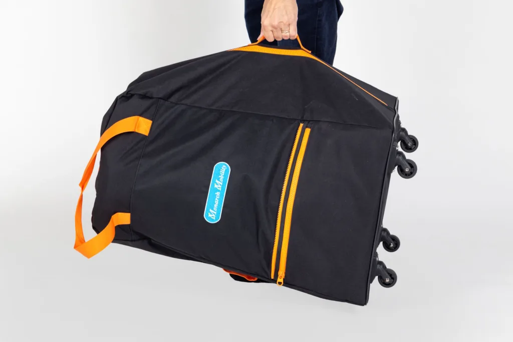 a close up a hand carrying a black and orange mobility scooter travel bag with wheels.