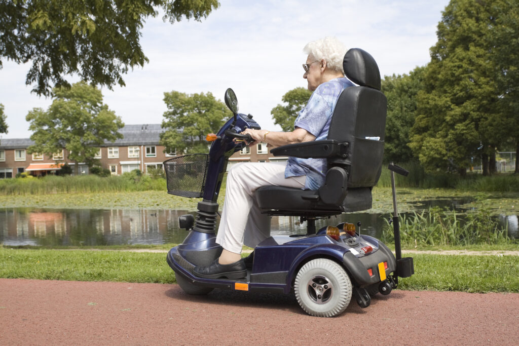 Elderly lady riding her mobility scooter alongside a lake