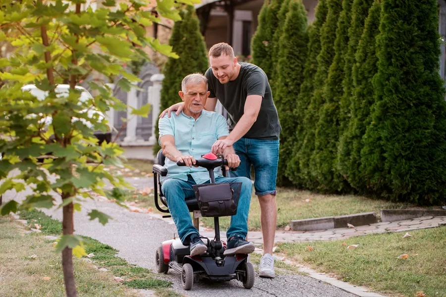 Young man on a path showing an older man how to use his mobility scooter