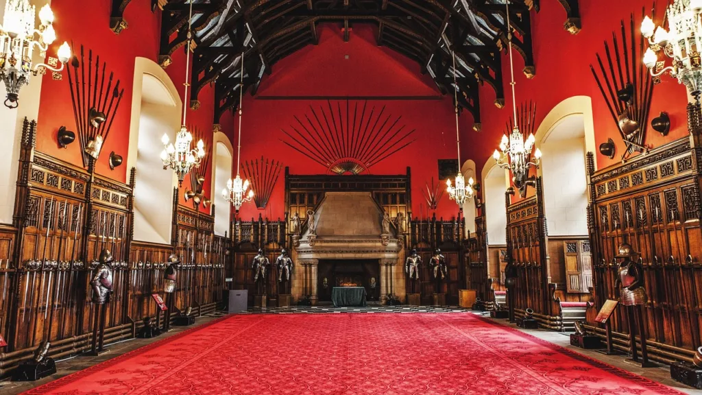 A red room in the castle with armoury on the walls and armour standing on the floor