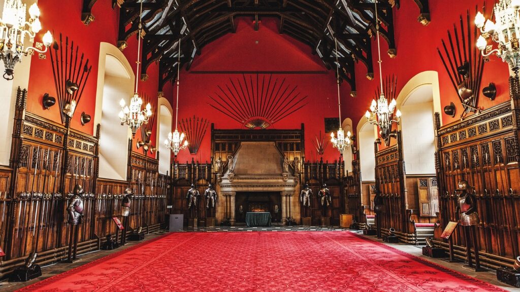 A red room in the castle with armoury on the walls and armour standing on the floor