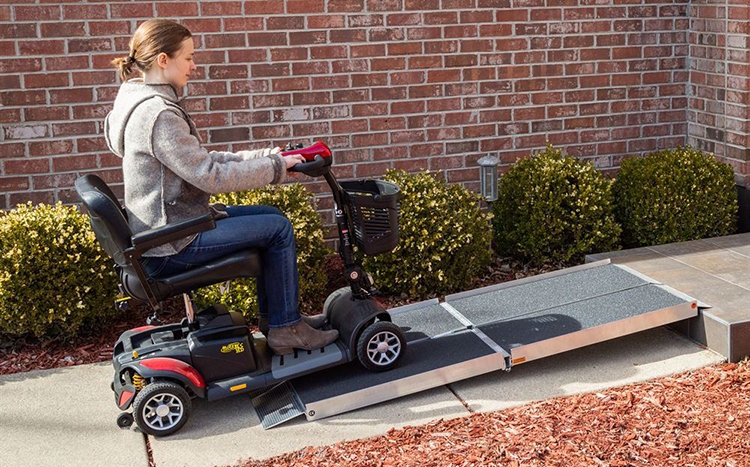 Lady driving a mobility scooter up a ramp that is placed over a step